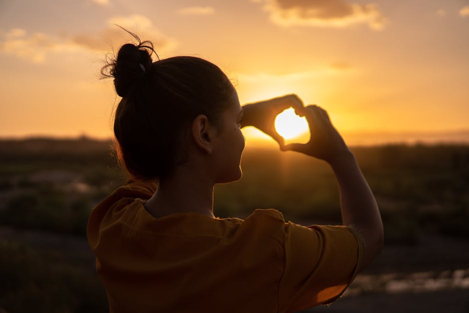 A silhouette of a young woman forming a heart shape at sunset in Kelâat M'Gouna, Morocco.